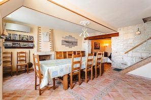 A dining area with a table set for six, wooden chairs, a brick wall, and a stone staircase. - Holiday Home 'L'Aixoise' with Private Terrace, Private Garden and Wi-Fi (Romegoux)
