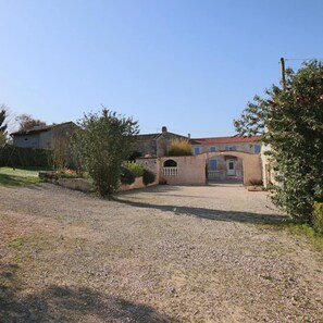 A two-story building with a gravel driveway, a small garden, and a red-tiled roof.