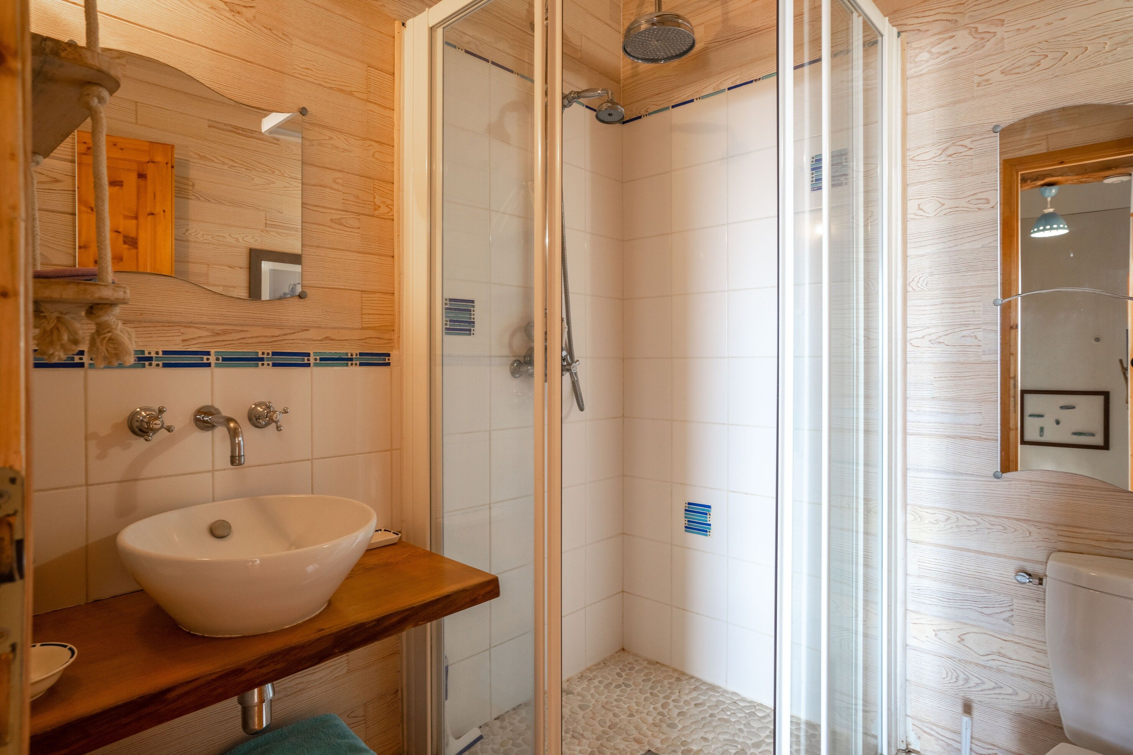 Ein Badezimmer mit einem Holzanrichte, einem weißen Waschbecken, einer Duschkabine aus Glas und einer Holzwandverkleidung.