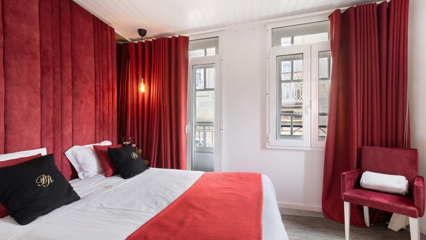 A hotel room with a bed, red curtains, a red chair, and a window with a view. - Apartment 'Prestigegoldresidence 2 - Old Town' with Balcony, Wi-Fi and Air Conditioning (Guimarães)