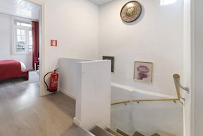 A hotel room with a bed, a fire extinguisher, a clock, and a framed picture on the wall.