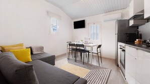 A modern living room with a sofa, a dining table with chairs, a kitchen area with a stove and cabinets, and a flat-screen TV mounted on the wall. - Apartment 'Prestigegoldresidence 2 - Old Town' with Balcony, Wi-Fi and Air Conditioning (Guimarães)