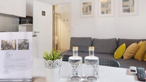 A living room with a sofa, a table with two bottles, a remote control, and a potted plant. - Apartment 'Prestigegoldresidence 2 - Old Town' with Balcony, Wi-Fi and Air Conditioning (Guimarães)