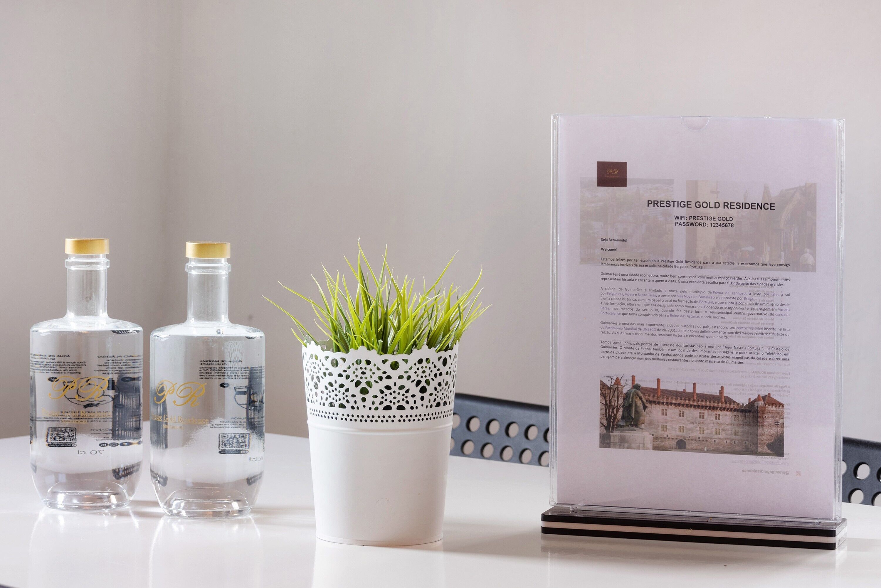 Two bottles of Prestige Gold Residence, a white decorative pot with green grass, and a framed informational sign.