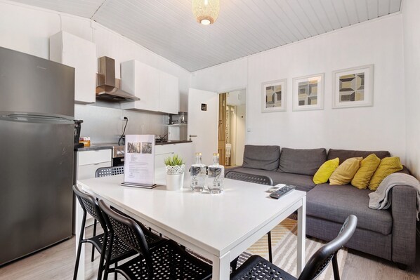 A modern kitchen with a refrigerator, white cabinets, and a dining table with chairs.