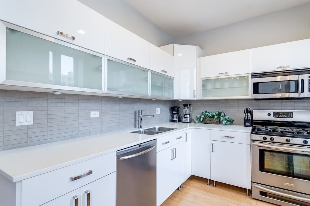 A modern kitchen with white cabinets, a stainless steel dishwasher, a double oven, and a microwave.