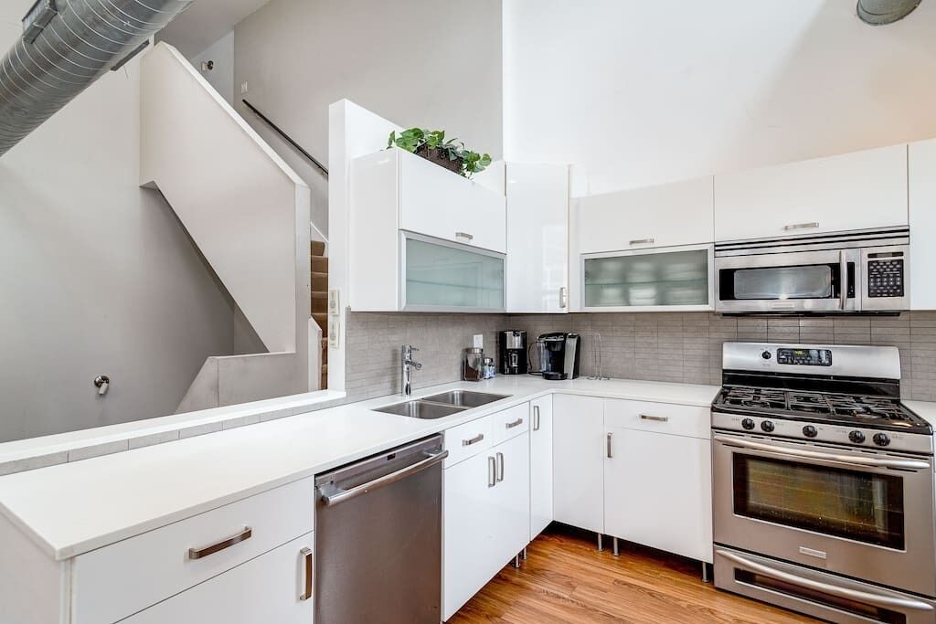 Una cocina moderna con armarios blancos, electrodomésticos de acero inoxidable, lavavajillas y horno empotrado.