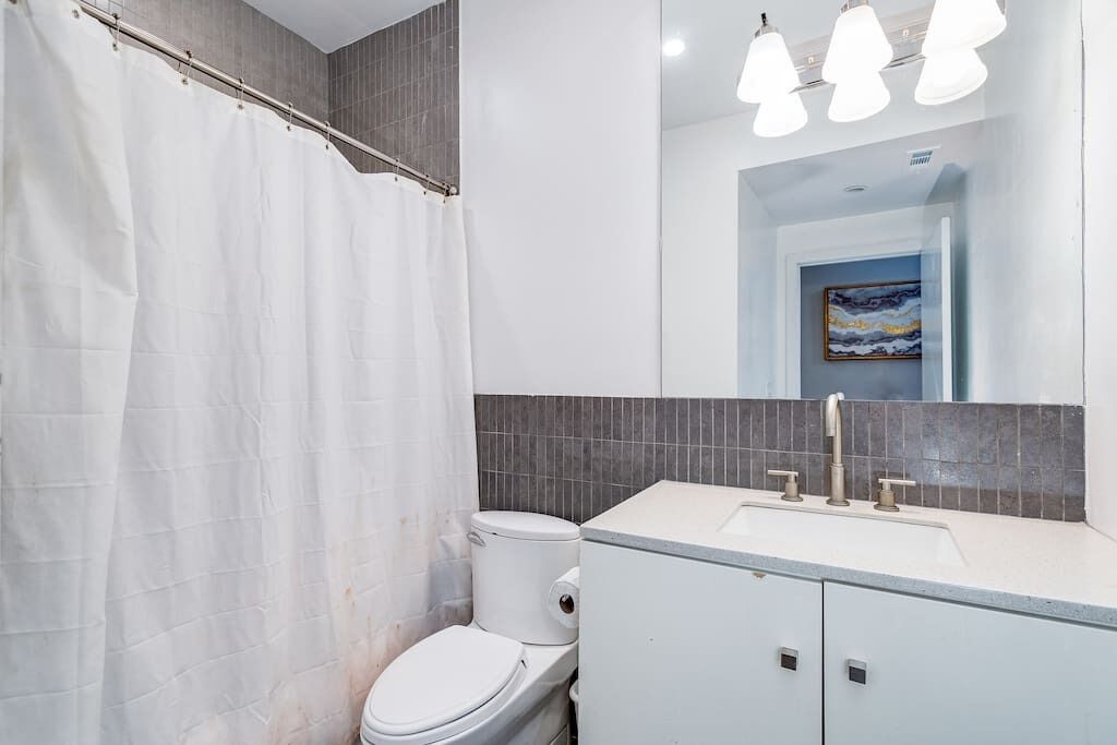 A modern bathroom with a white toilet, a shower curtain, a sink with a mirror above it, and a ceiling light fixture.