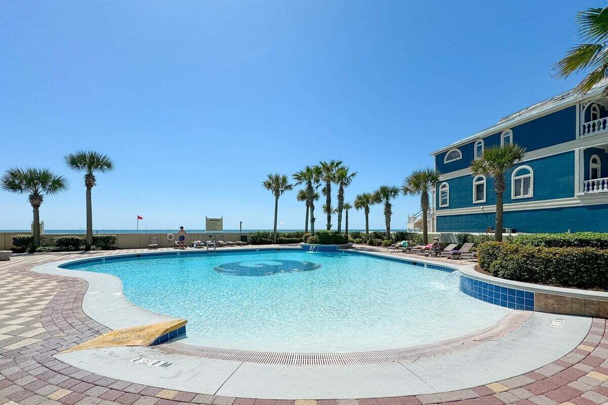 Una piscina de diseño circular, rodeada de palmeras y un edificio con fachada azul.