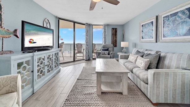 A living room with a television, sofa, coffee table, and a view of the beach through a sliding glass door.