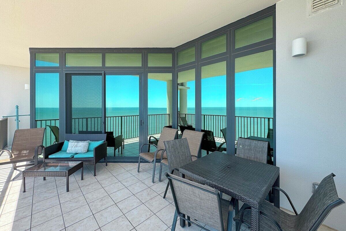 A balcony with a view of the ocean, furnished with chairs and a table.