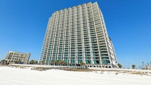 A tall, modern hotel with multiple floors and balconies, situated near a beach.
