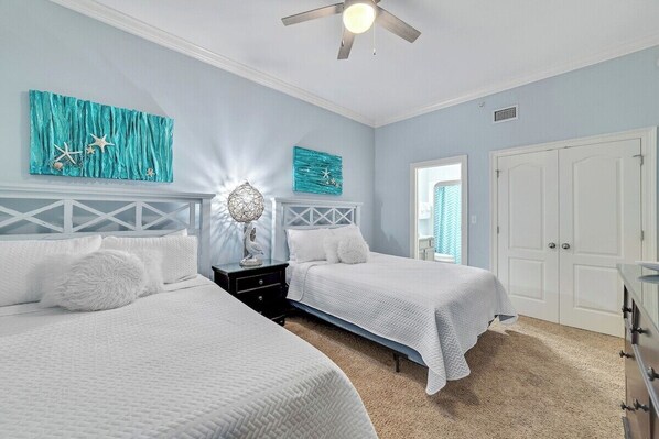 A bedroom with two beds, a ceiling fan, and artwork on the walls.