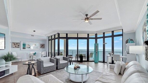 A spacious living room with a glass coffee table, white sofas, and a view of the ocean through large windows.