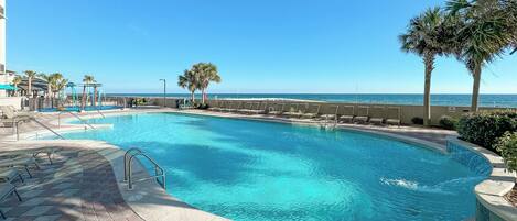 Une piscine offrant une vue dégagée sur l’océan, entourée de palmiers et dotée d’une terrasse dallée.