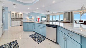 A spacious kitchen with light blue cabinets, a dishwasher, and a large island with a marble countertop. - ULTRA LUXURY BEACHFRONT CONDO, 3500SQFT, CUSTOM EVERYTHING (Orange Beach)