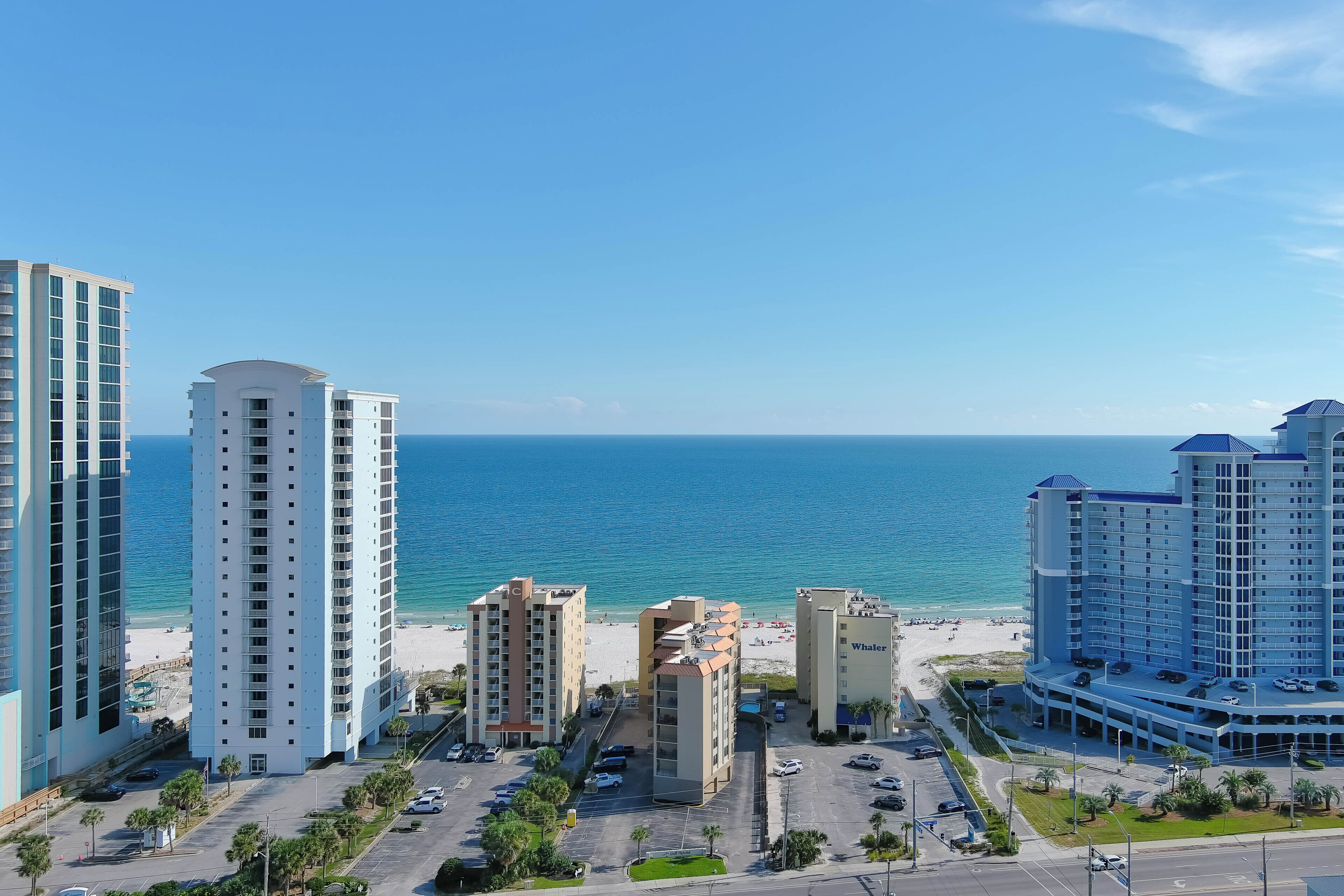 A coastal cityscape with high-rise buildings, a beach, and a parking area.
