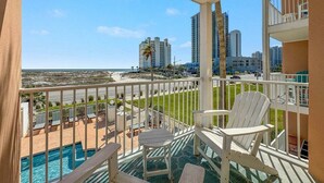 Un balcón con vista a la playa y al océano, sillas blancas y una piscina.