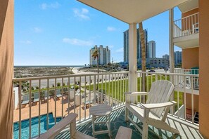 Un balcon avec vue sur la plage et l’océan, des chaises blanches et une piscine.