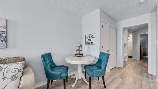 Una habitación con una mesa redonda blanca, dos sillas azul verdosas, una puerta blanca y una pared con el letrero 'RELAX AND UNWIND'.