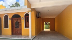 A corridor with a yellow wall, a wooden door with glass panels, and a ceiling fan. - Kiimakóol  (Coba)
