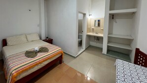 A bedroom with a bed, a bedside table, and a small table with a patterned tablecloth. - Kiimakóol  (Coba)