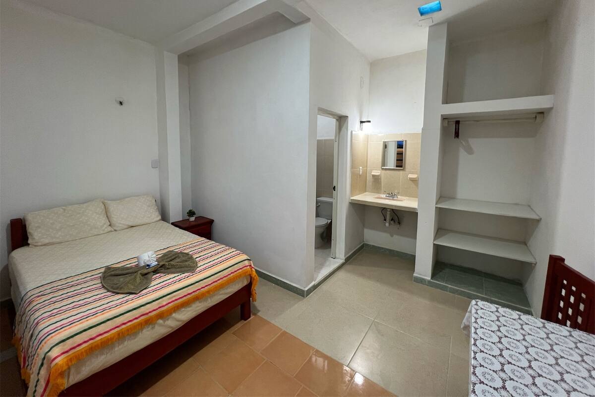 Un dormitorio con una cama, una mesita de noche y una pequeña mesa con mantel estampado.