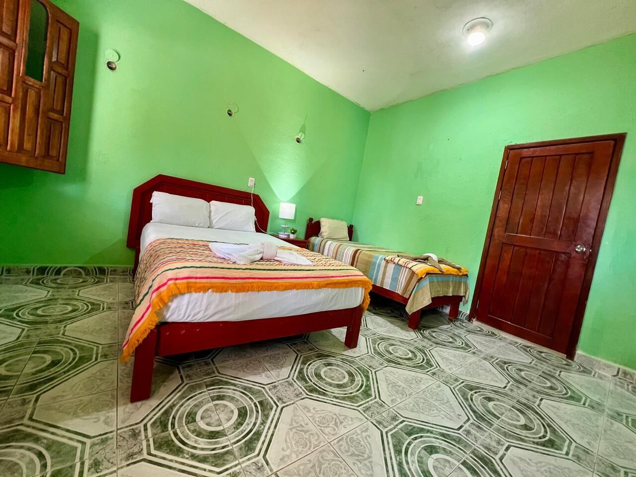 Una habitación con paredes verdes, una cama roja y un suelo estampado.