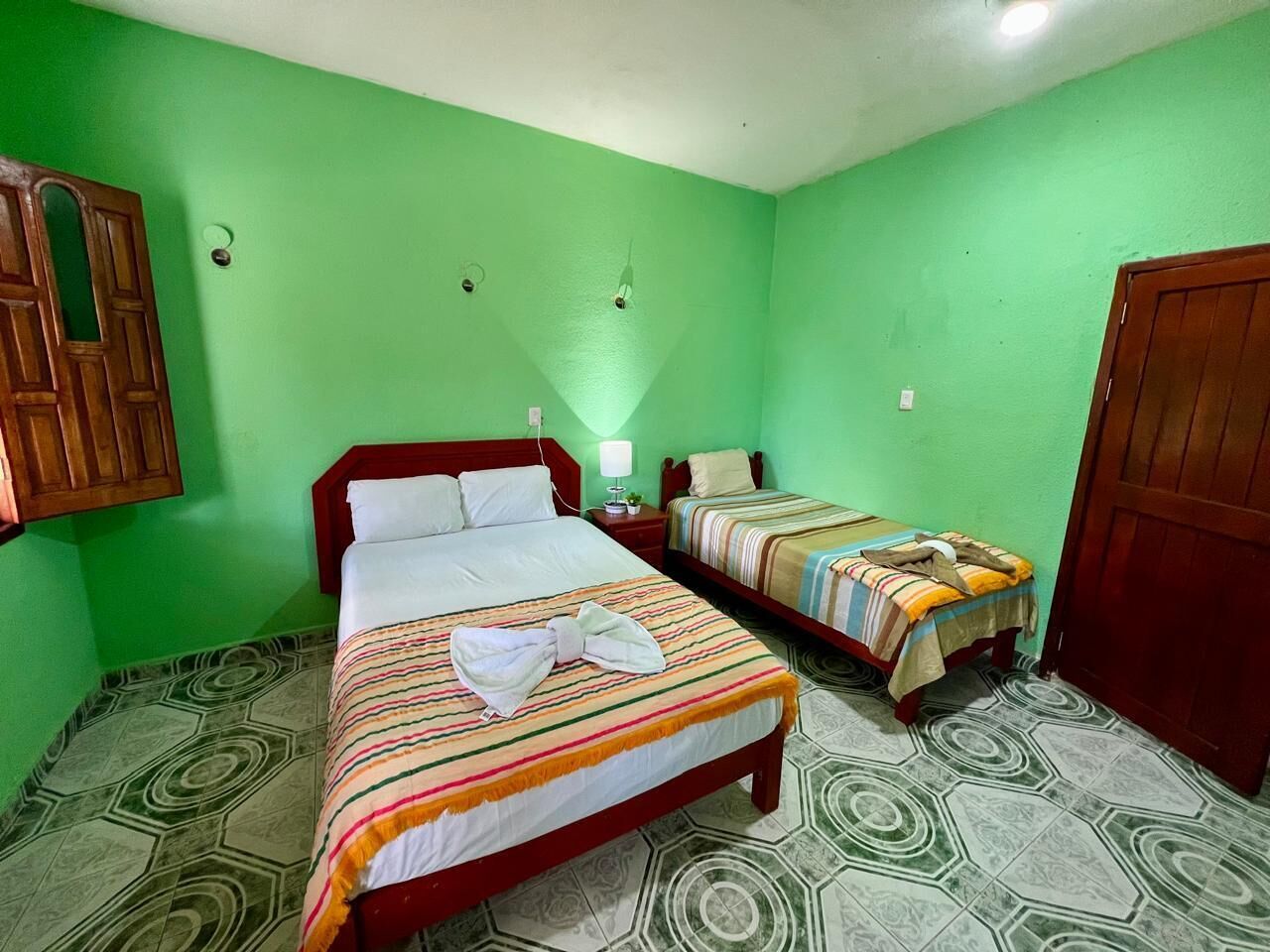 Una habitación con dos camas, paredes verdes y suelo estampado.