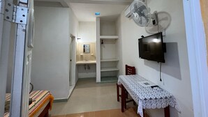 A small, well-lit room with a TV mounted on the wall, a table with a lace tablecloth, and a chair. - Kiimakóol  (Coba)