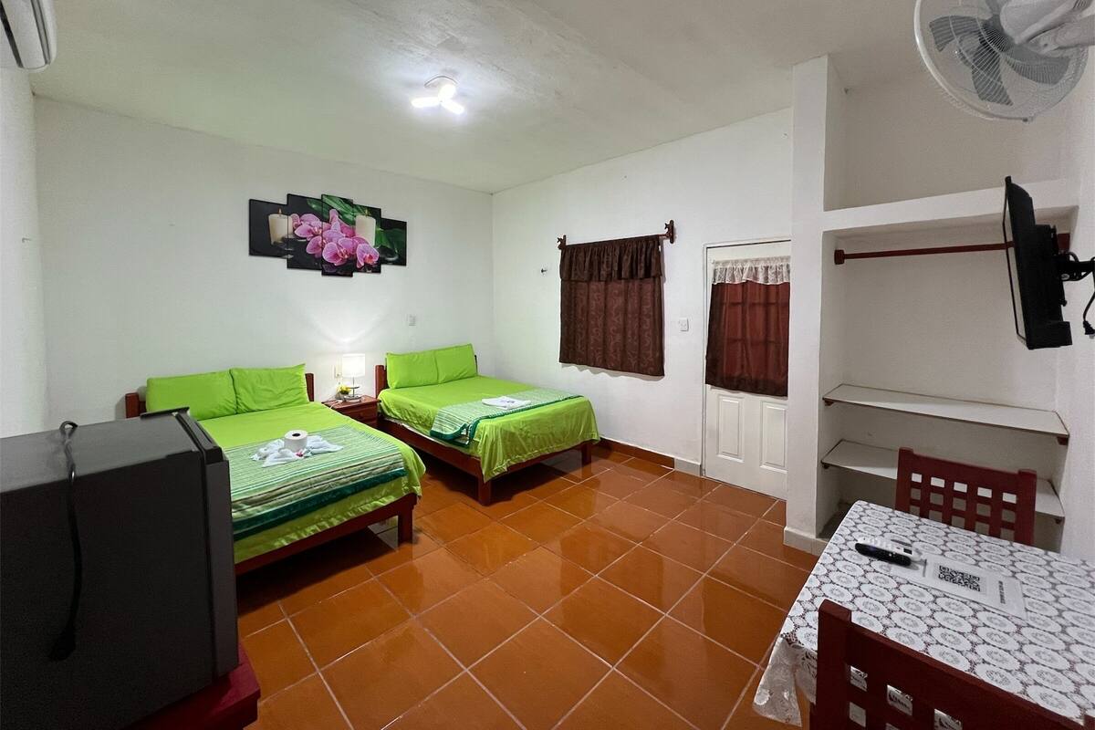 Una habitación con dos camas, una mesa, un ventilador y un televisor.