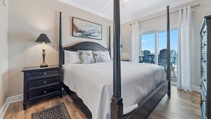 A four-poster bed with a dark headboard, a bedside table with a lamp, a large window with curtains, and a view of the outdoors. - AMAZING CORNER UNIT, HUGE POOLS, BEACH VIEWS - Crystal Tower 809 (Gulf Shores)