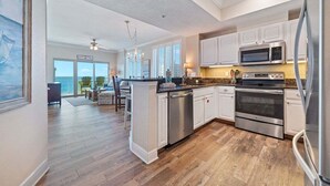 A modern kitchen with white cabinets, stainless steel appliances, and a wooden floor. - AMAZING CORNER UNIT, HUGE POOLS, BEACH VIEWS - Crystal Tower 809 (Gulf Shores)