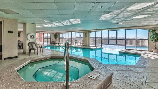An indoor swimming pool with a hot tub, surrounded by lounge chairs and a view of the city skyline. - BEACHFRONT, FAMILY FRIENDLY, LOW FLOOR, OUTDOOR POOL (Orange Beach)