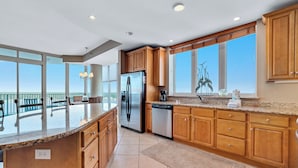 A modern kitchen with wooden cabinets, a stainless steel refrigerator, and a large island. - WATERFRONT LOW DENSITY CONDO, BEACH ACCESS, INDOOR/OUTDOOR POOLS (Gulf Shores)