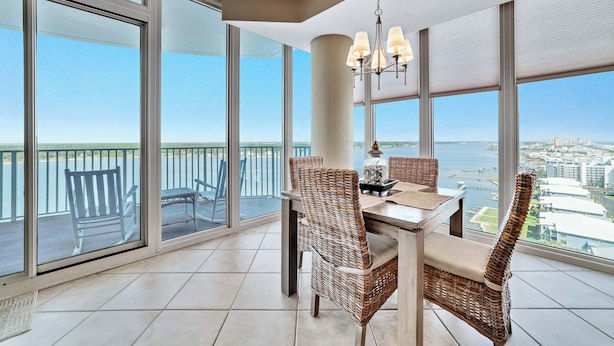 A balcony with a dining table and wicker chairs, large windows with a city view, and a hanging light fixture. - WATERFRONT LOW DENSITY CONDO, BEACH ACCESS, INDOOR/OUTDOOR POOLS (Gulf Shores)
