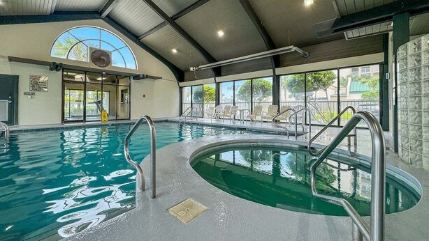 Una piscina interior con agua cristalina, escaleras de metal y un amplio ventanal en arco.