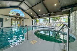 An indoor swimming pool with clear water, metal ladders, and a large arched window.