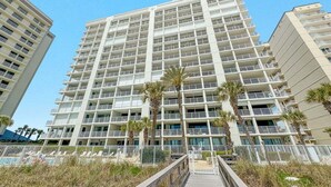 Un hotel de varios pisos con balcones, un área de piscina y palmeras.