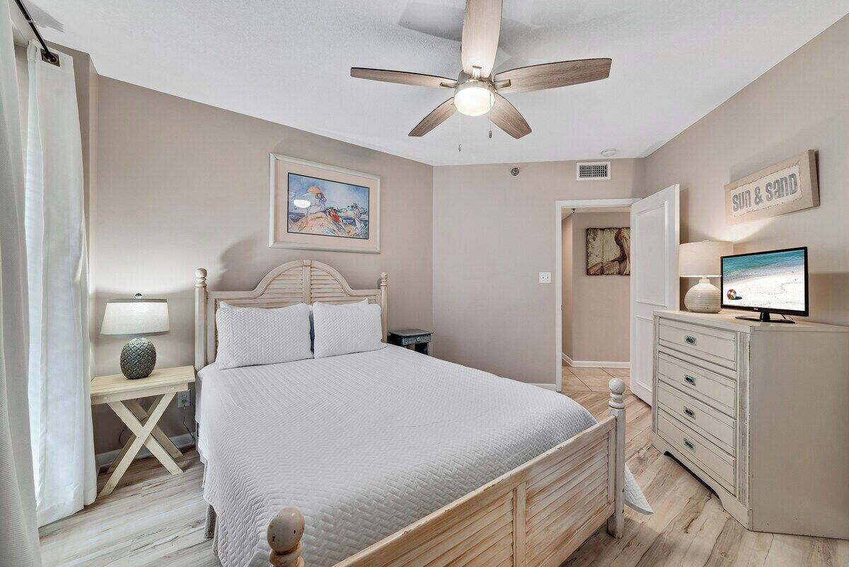 Une chambre à coucher comprenant un lit, un ventilateur de plafond, une table de chevet avec une lampe, une commode et un téléviseur.