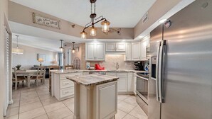 Una cocina moderna con armarios blancos, una isla central, electrodomésticos de acero inoxidable y una lámpara decorativa en el techo.