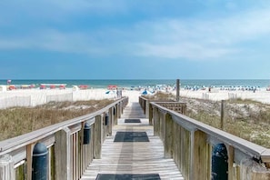 A wooden boardwalk leading to a beach with umbrellas and beachgoers. - Shoalwater 104 - Private Patio Gate to Pool & Beach - Beachball Properties (Orange Beach)