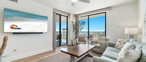 A modern living room with a large TV, a ceiling fan, a dining table, and a sofa.