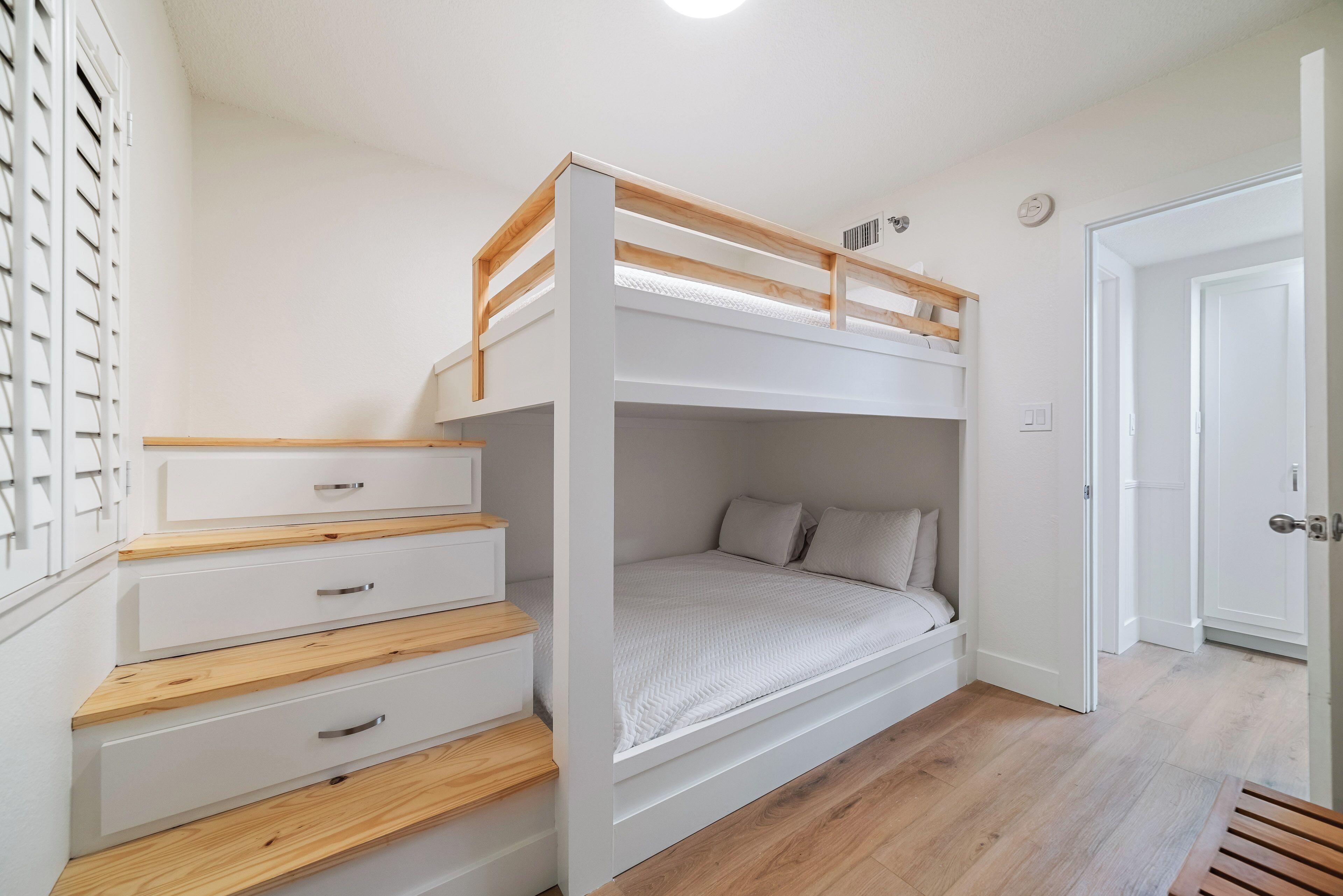 Un letto a castello con testiera in legno, cassetti bianchi e materasso bianco.