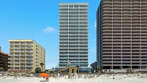 A beachfront hotel with multiple floors, a sandy beach in the foreground, and a clear blue sky. - BEACHFRONT, LOW DENSITY CONDO, CORNER UNIT, CLOSE TO RESTAURANTS - The Colonnades 703 (Gulf Shores)