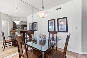 A dining area with a glass table surrounded by wooden chairs, a hanging light fixture, and framed artwork on the walls.