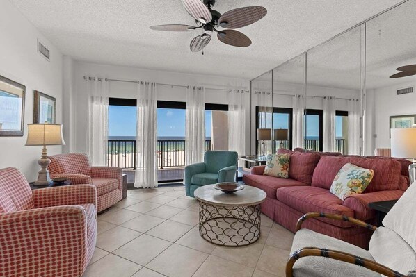 A spacious living room with a large window, a ceiling fan, and a red sofa.