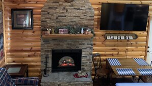 A cozy cabin interior with a stone fireplace, wooden walls, a television, and a checkered table.