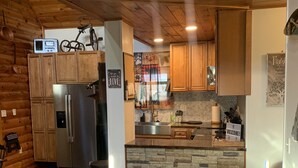 A cozy cabin-style kitchen with wooden cabinets, a stone backsplash, and a built-in refrigerator.