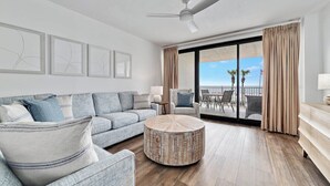 A modern living room with a grey sofa, round coffee table, and a balcony with a view of the ocean.